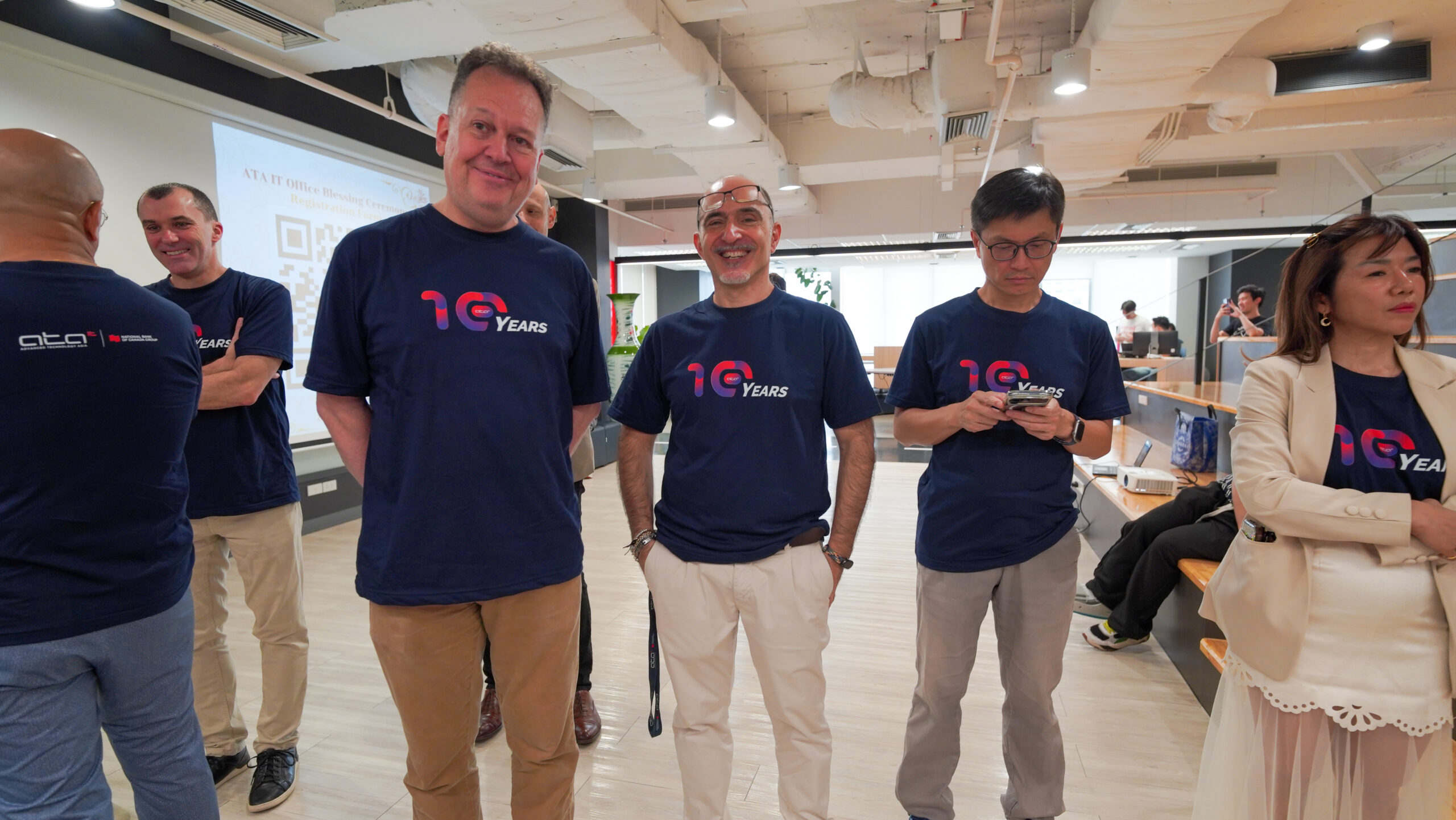 Group of people in navy blue '10 Years' shirts standing together in a bright office or event space.