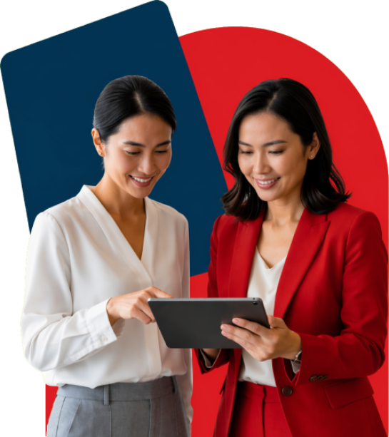 Two businesswomen collaborate, looking at a tablet together in front of a blue and red abstract background.